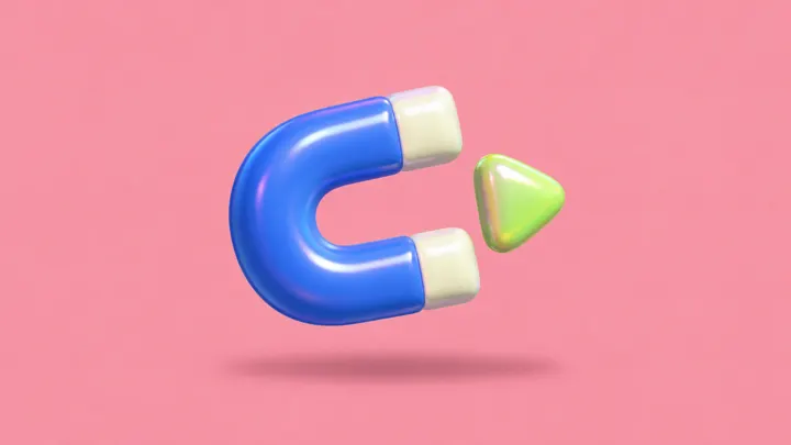 Um ímã inflável azul atrai uma pequena pedra verde em forma de botão de play, sobre fundo rosa.