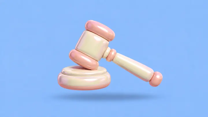 Um martelo de juiz inflável creme e rosa apoiado sobre sua base, sobre fundo azul-claro.