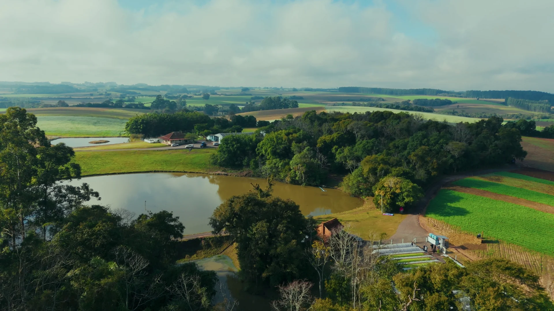 Vista aérea de propriedade rural com açude, mata nativa e lavouras em diferentes tons de verde.