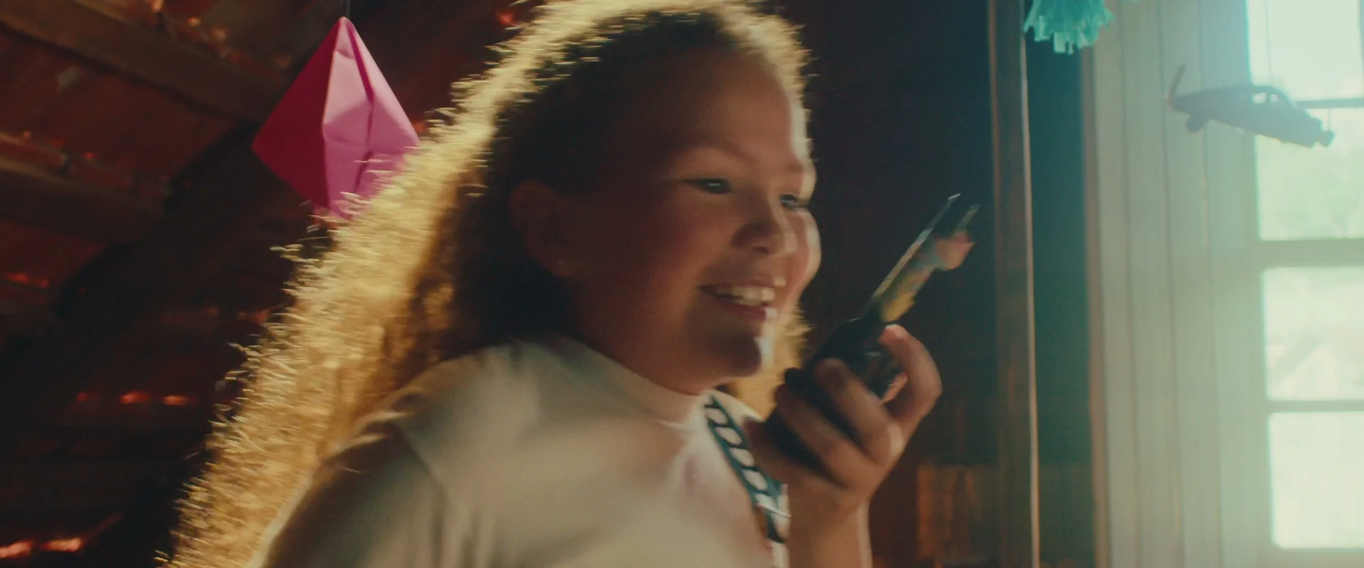 Menina contra a luz da janela do sótão fala num walkie-talkie e sorri.