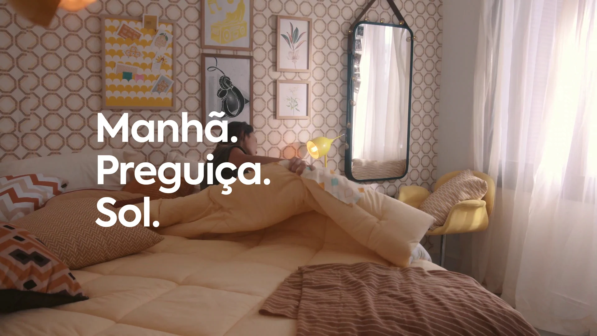 Quarto com papel de parede geométrico dourado e cama desarrumada, com a cartela Manhã. Preguiça. Sol.