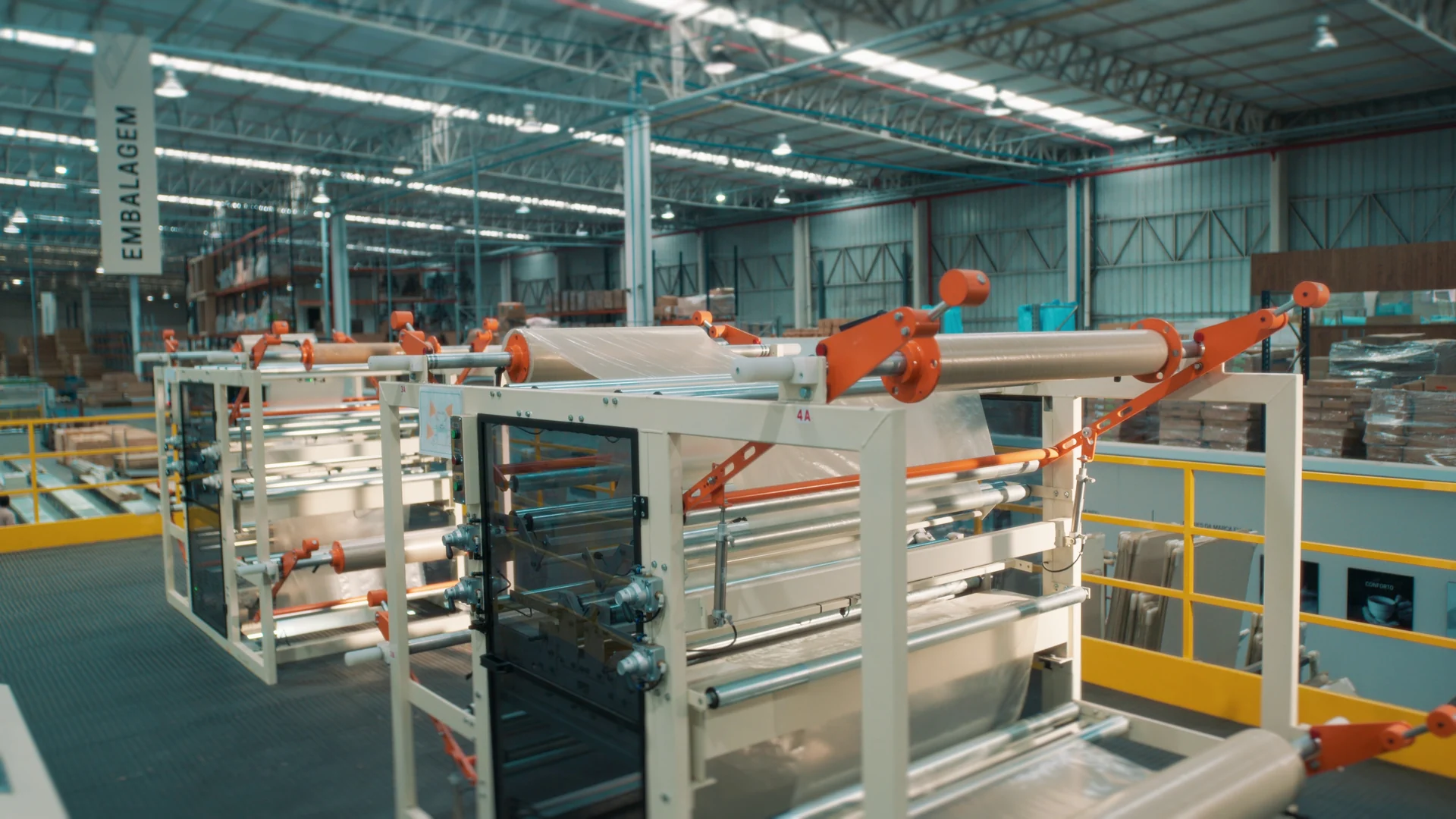 Linha de produção ampla com estruturas brancas e laranja, trilhos amarelos e pé-direito alto.