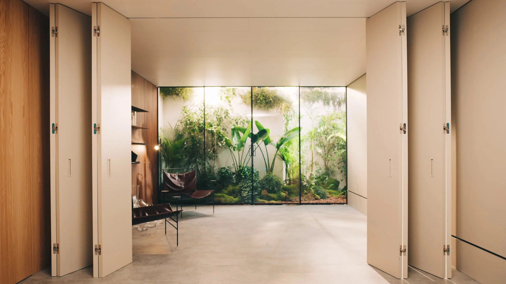 Portas brancas dobráveis abertas integram o ambiente interno a um jardim envidraçado.