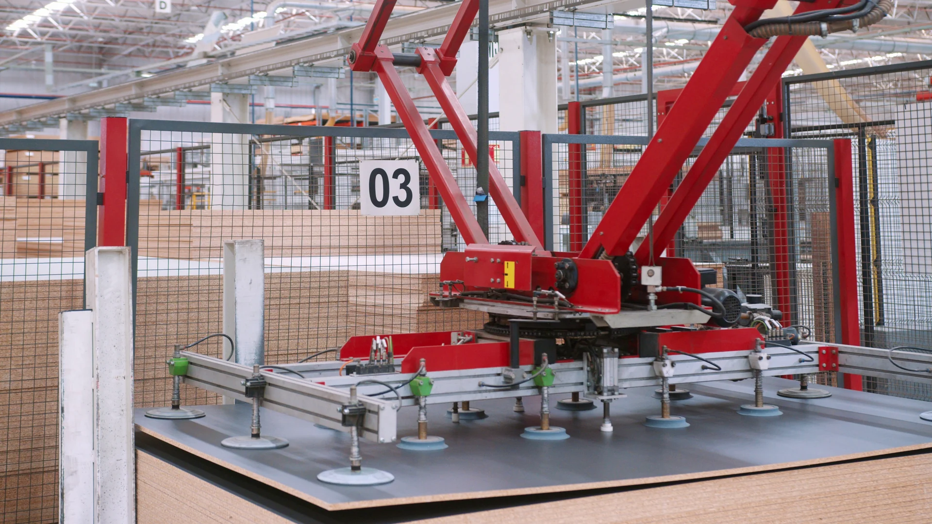 Braço robótico vermelho com ventosas movimenta uma chapa de madeira dentro de uma célula automatizada da fábrica.