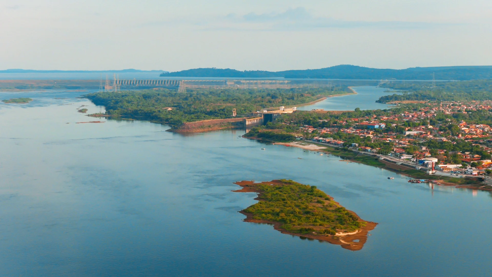Vista aérea de um rio largo com uma pequena ilha em primeiro plano e a cidade na margem, em luz de fim de tarde.