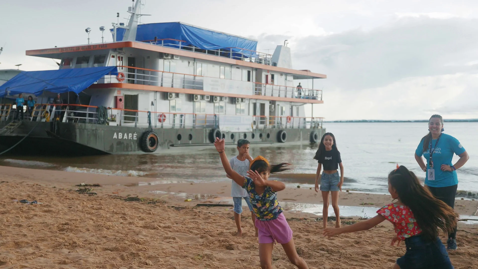 Crianças brincam na areia da margem em frente ao navio Abaré, observadas por uma integrante da missão.