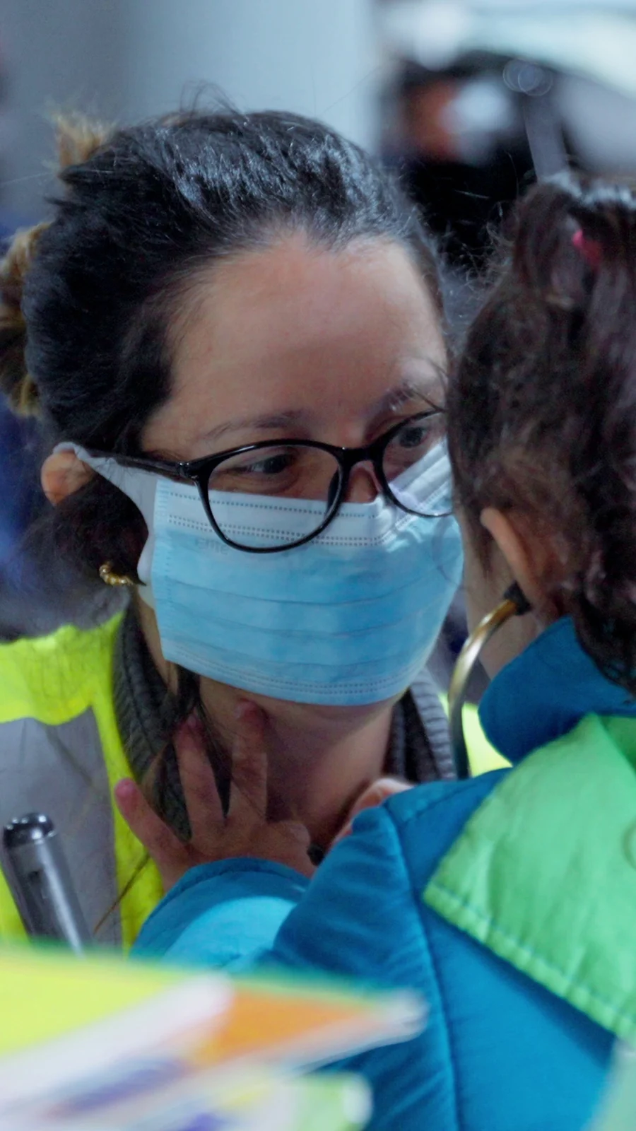 Voluntária de máscara e óculos em close, com uma criança encostada no ombro.