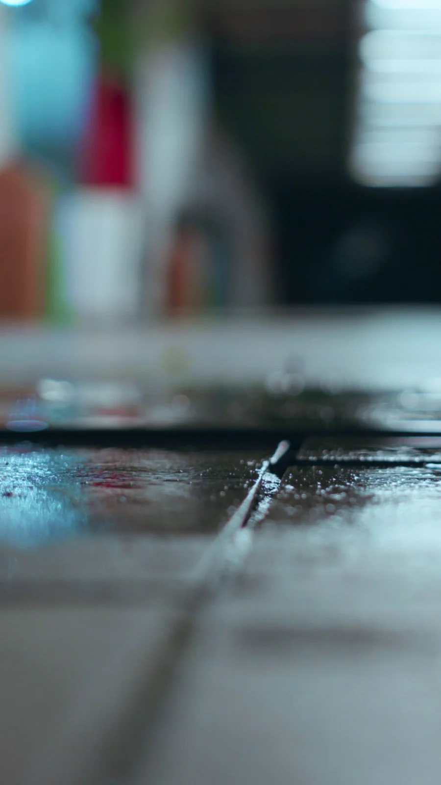 Detalhe em macro de água sobre um piso, com reflexos e luzes desfocadas.