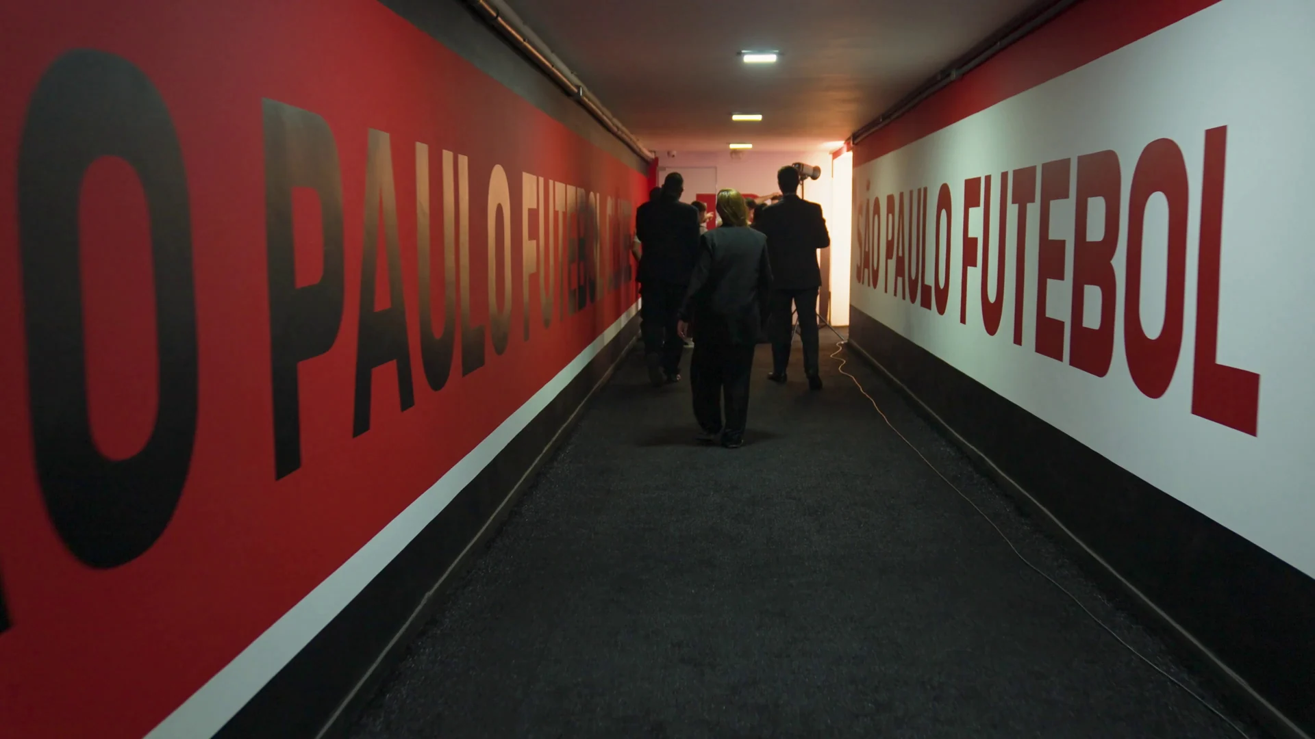 Túnel de acesso ao campo com o nome do clube em letras grandes pretas sobre parede vermelha e branca.