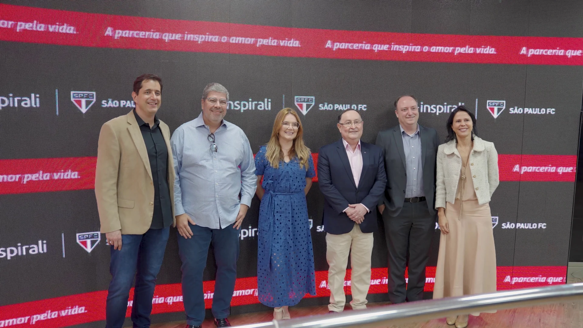 Seis pessoas posam lado a lado diante do painel da parceria Inspirali e São Paulo FC.