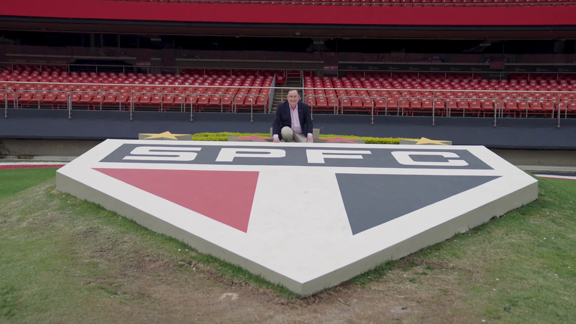 Escudo gigante do São Paulo FC em relevo no gramado, com as arquibancadas do estádio ao fundo.