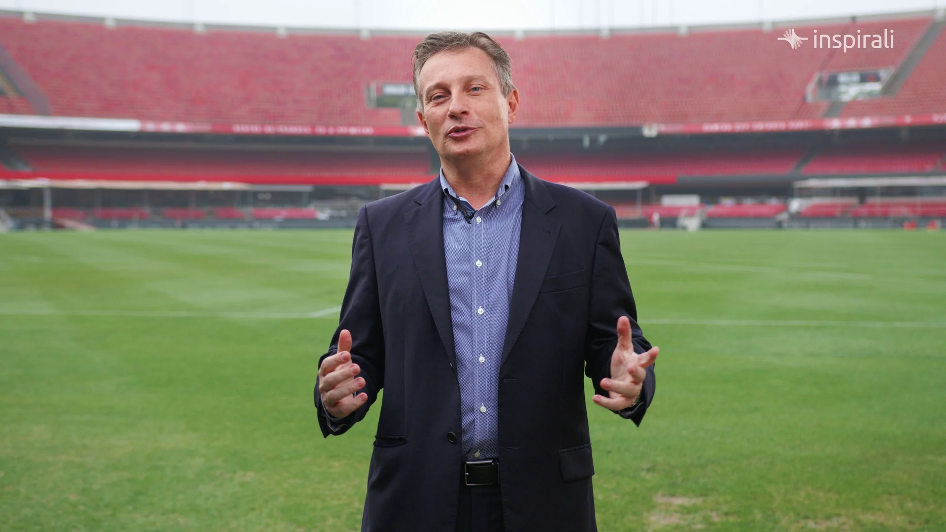 Médico de blazer azul fala para a câmera no gramado do Morumbi, com as arquibancadas desfocadas.