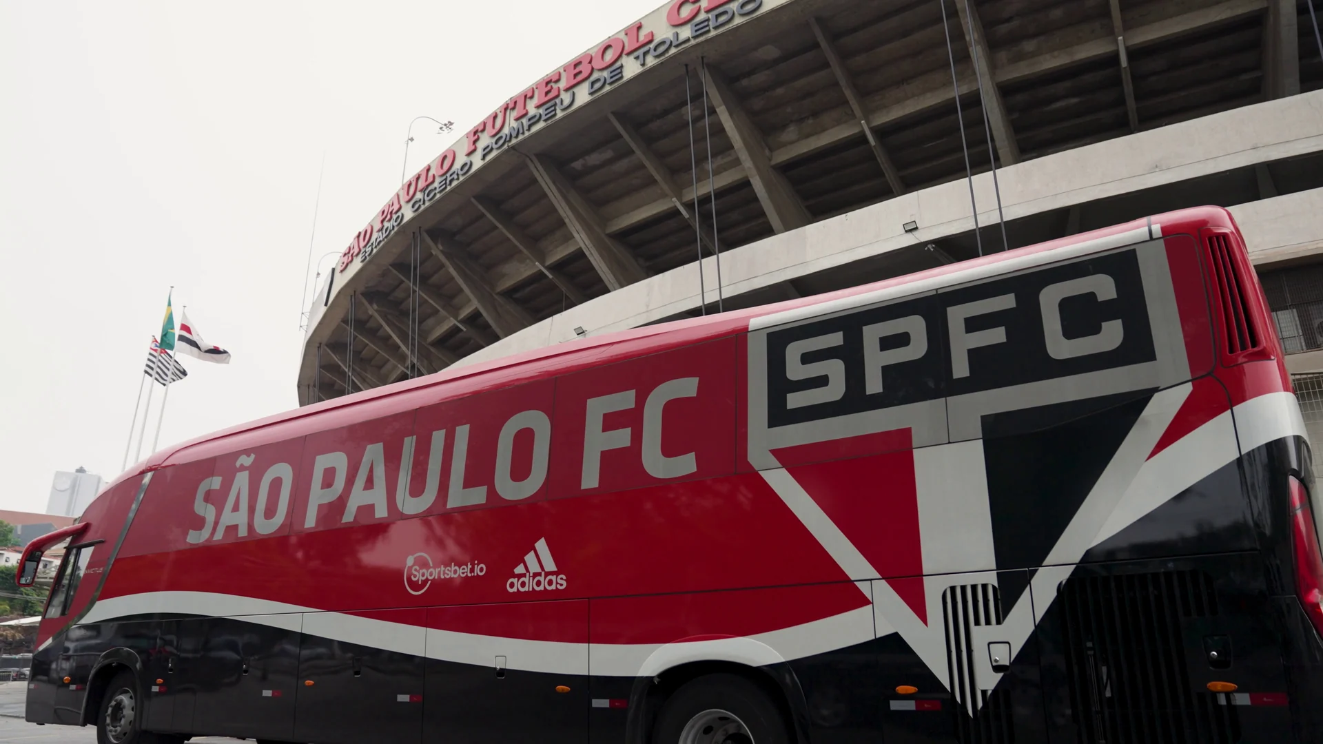 Ônibus vermelho e preto do São Paulo FC estacionado diante da arquibancada do Estádio do Morumbi.
