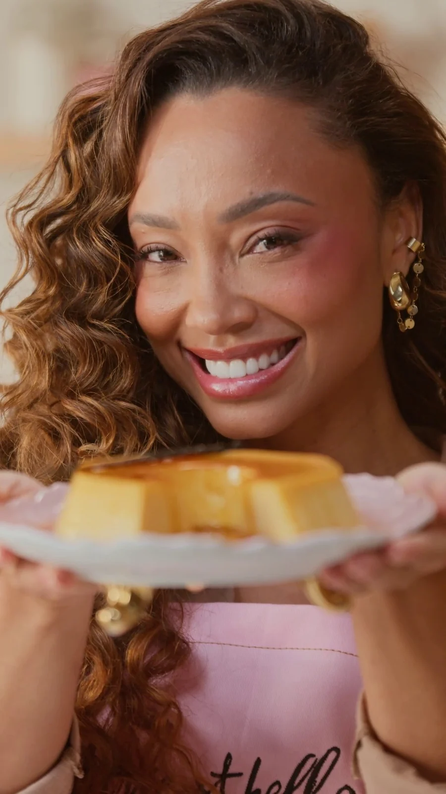 Michele Crispim sorri para a câmera segurando um prato com pudim de caramelo.