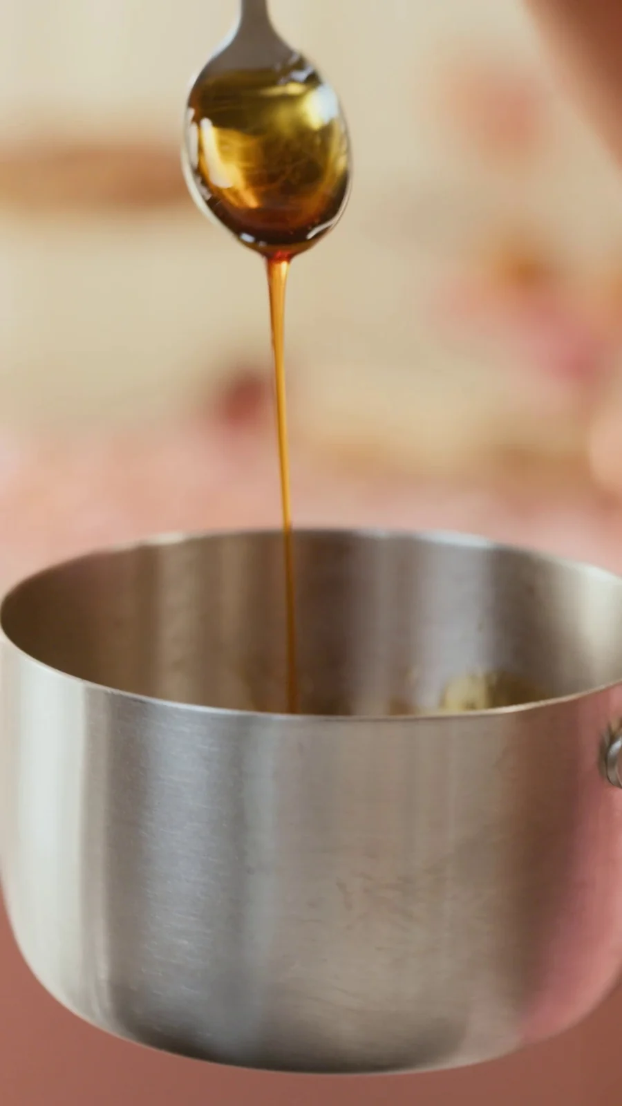 Uma colher deixa escorrer um fio de caramelo âmbar dentro de uma panela de inox.