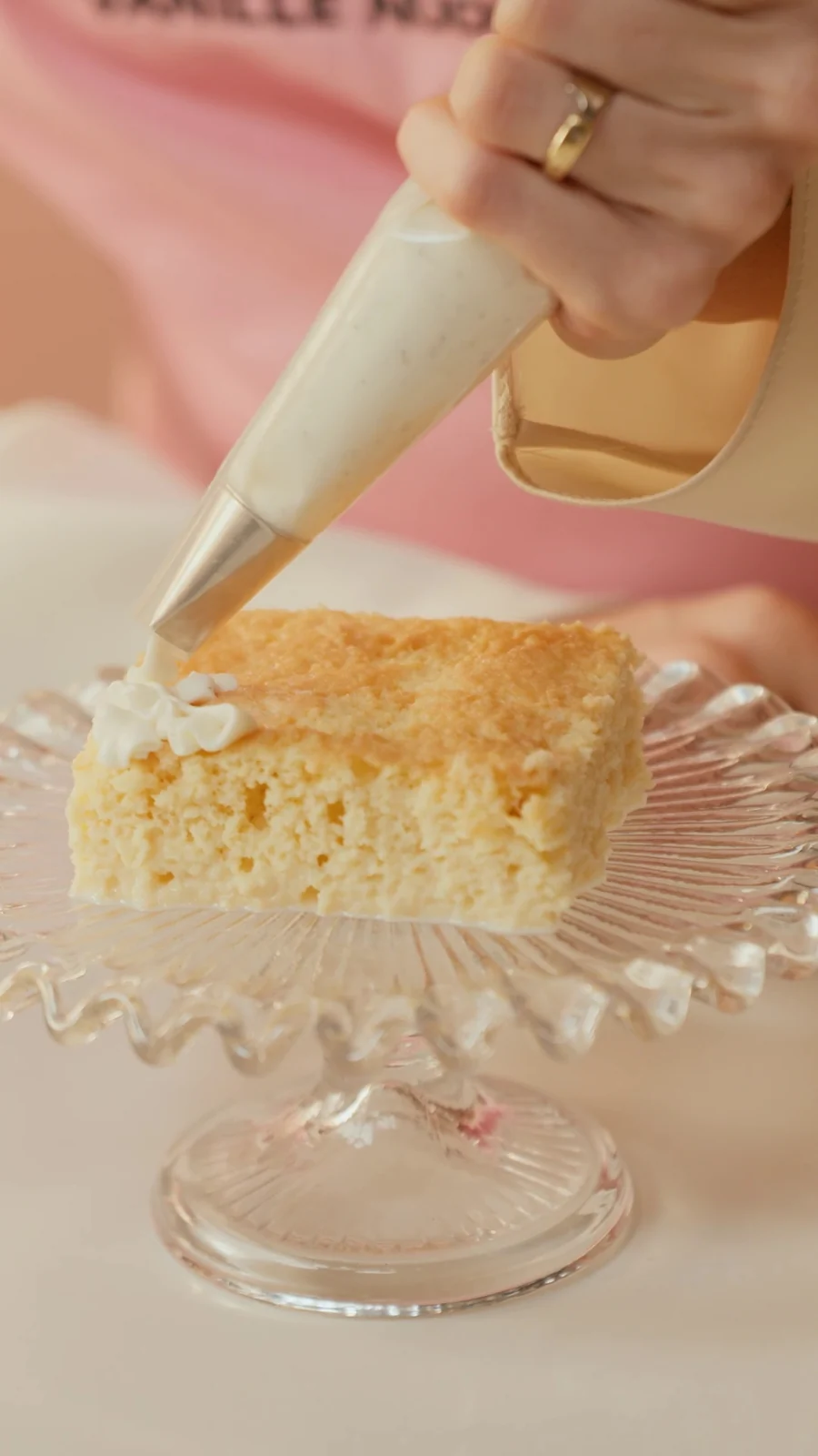 Saco de confeitar cobre de chantilly de baunilha uma fatia de bolo sobre uma boleira de vidro.