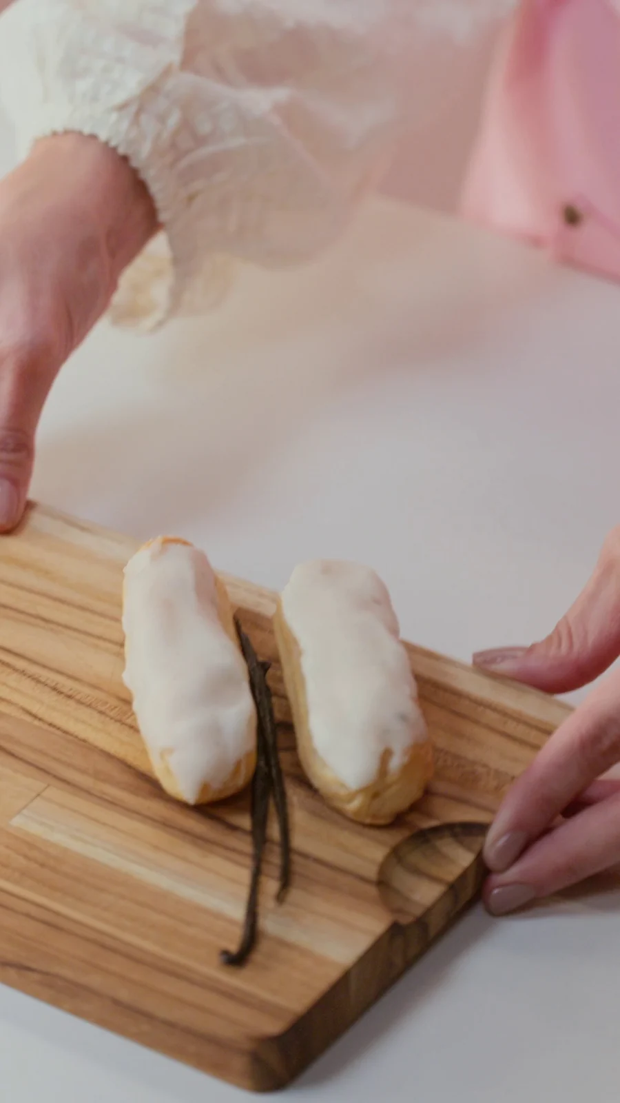 Duas éclairs com glacê branco e favas de baunilha sobre uma tábua de madeira.