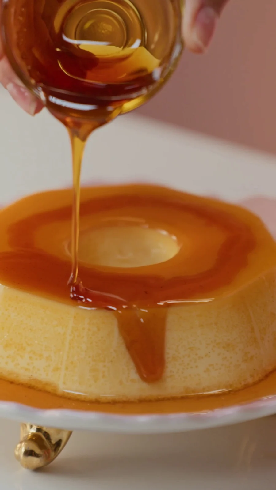 Calda de caramelo escorre sobre um pudim desenformado num prato branco.
