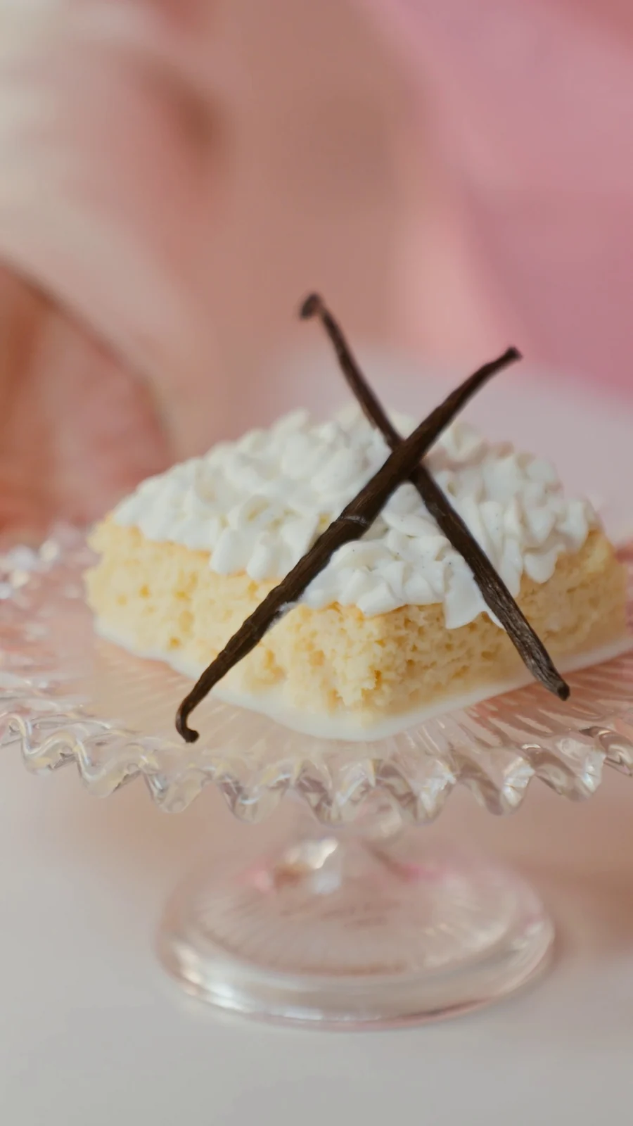 Fatia de bolo tres leches com chantilly e duas favas de baunilha cruzadas, sobre uma boleira de vidro trabalhado.