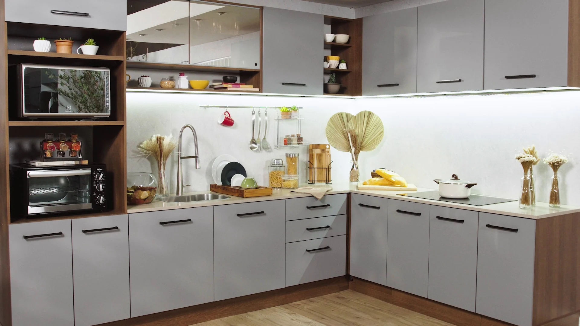 Cozinha em L com portas cinza e detalhes em madeira, torre com forno e micro-ondas e fita de LED sob os aéreos.