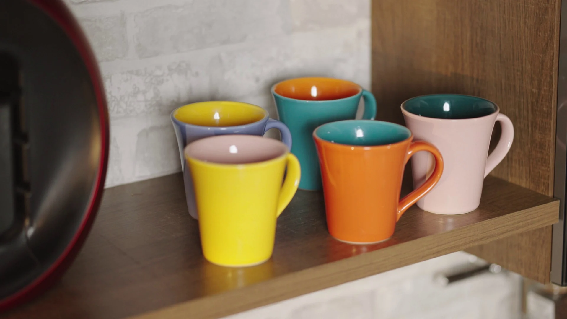 Canecas coloridas — amarela, azul, laranja e rosa — sobre prateleira de madeira de um módulo de cozinha.