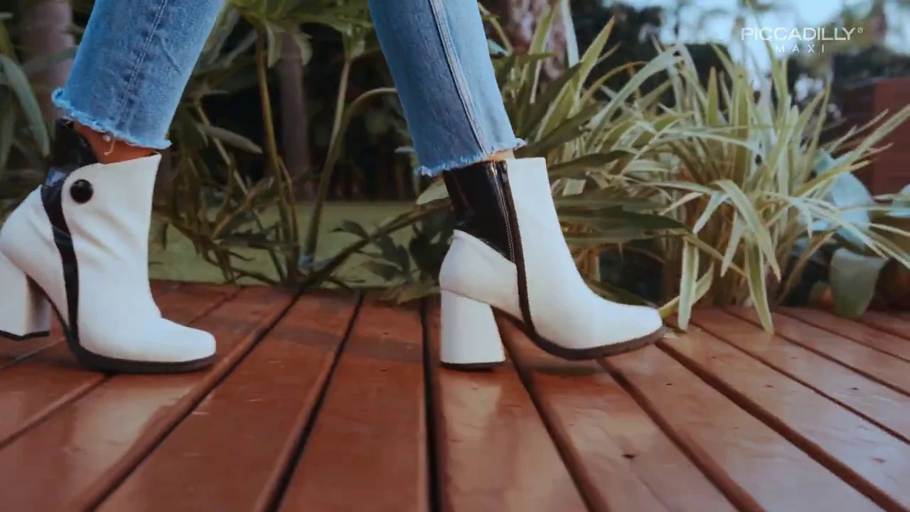 Botas brancas de cano curto e salto grosso caminham sobre deck de madeira.