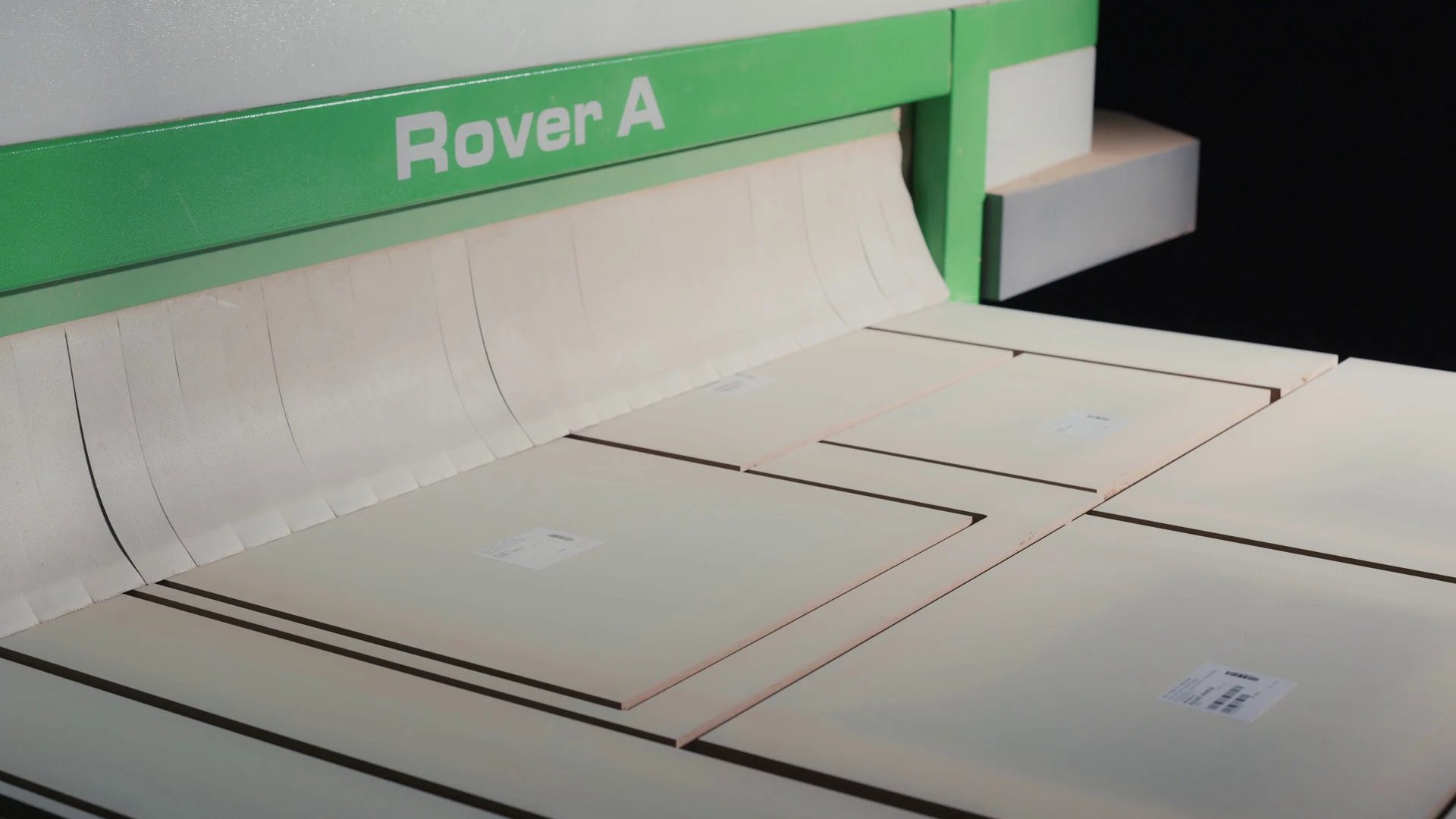 Painéis claros recortados sobre a mesa de uma máquina de corte industrial com a inscrição Rover A.