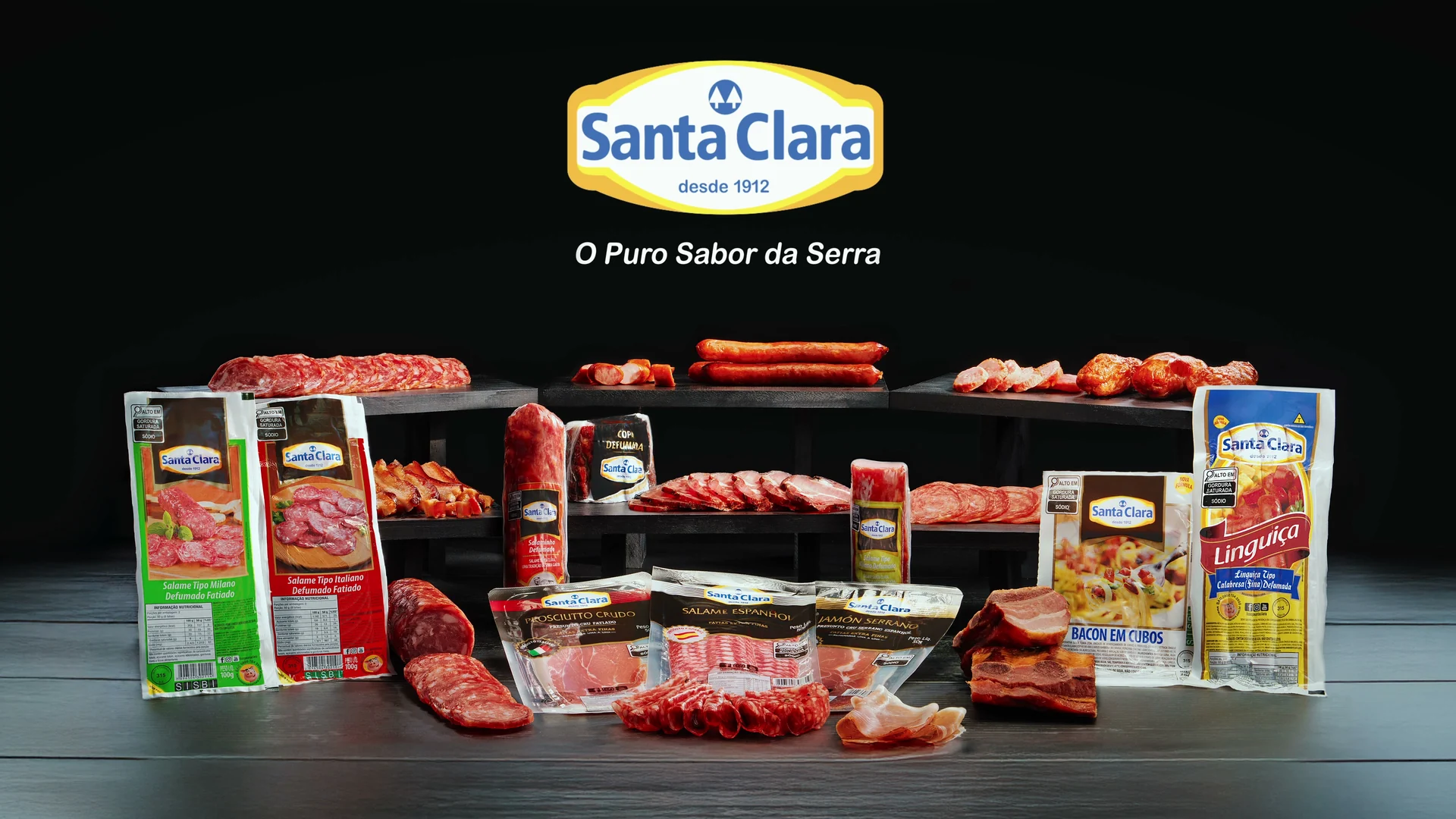 Packshot final: logo Santa Clara, desde 1912, e a linha de embutidos e fatiados embalados, sobre bancada escura.
