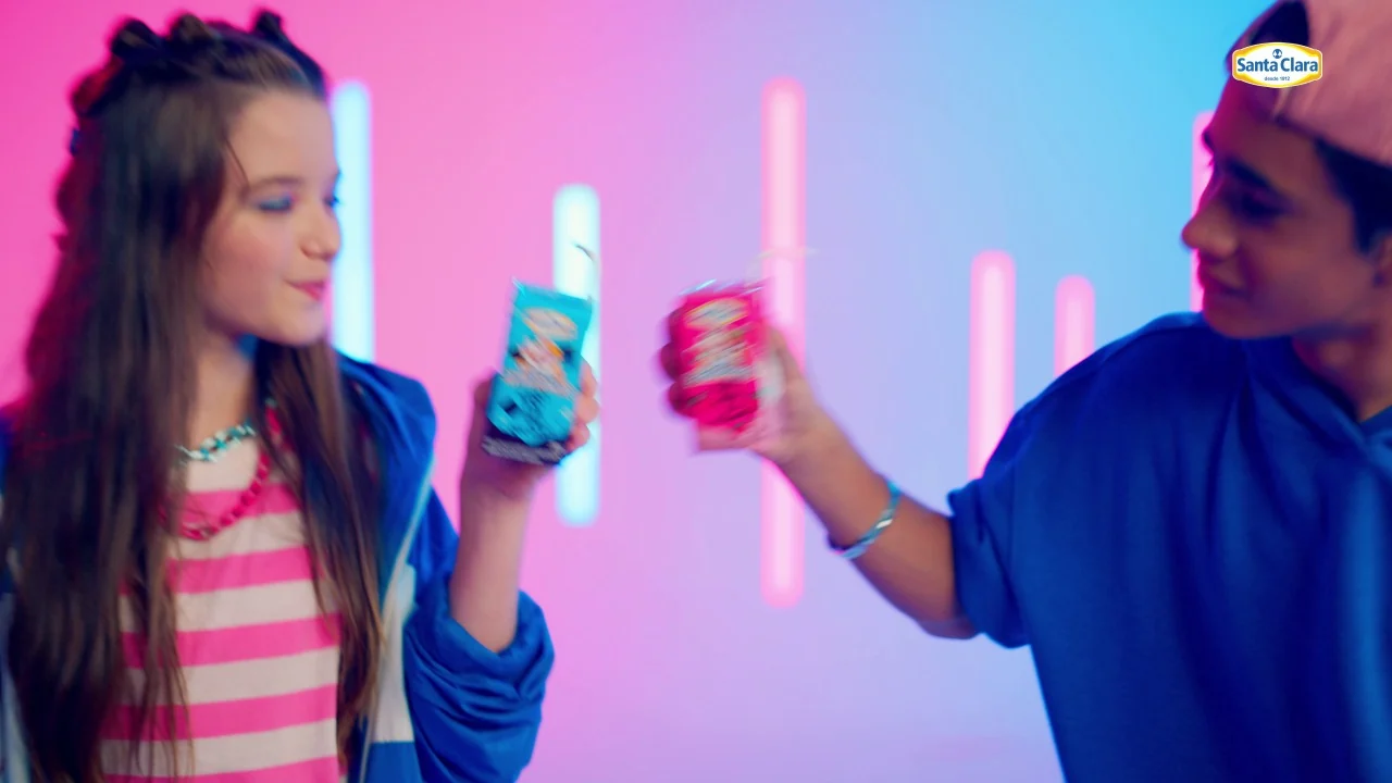 Menina e menino brindam com as caixinhas azul e rosa diante das luzes de neon.