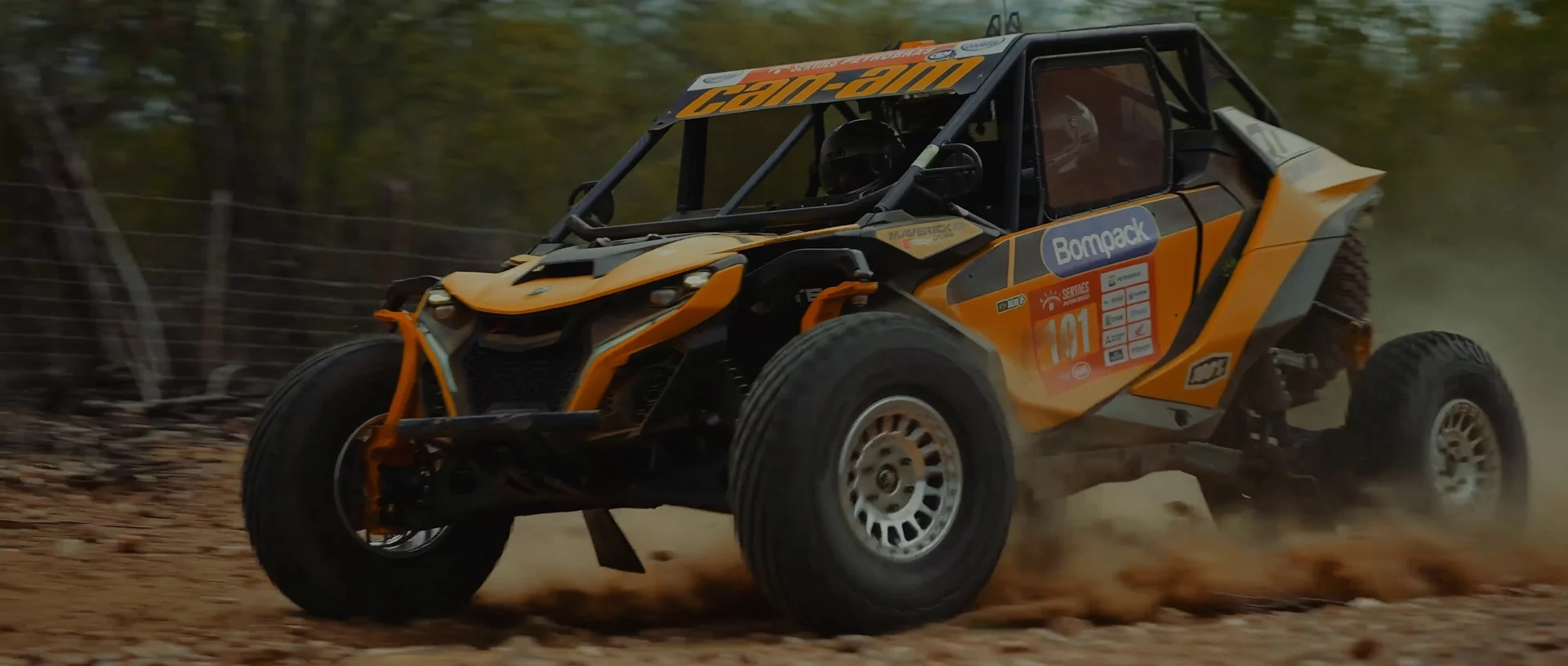 UTV laranja de rali acelera em estrada de terra levantando poeira.