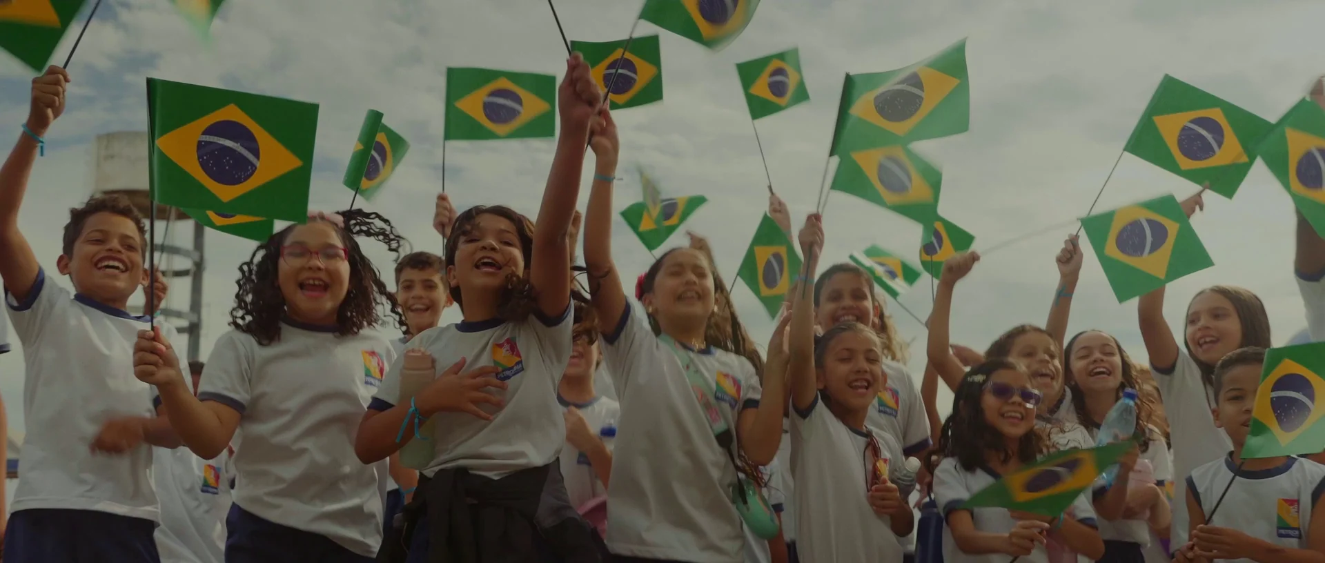 Crianças de uniforme escolar agitam bandeiras do Brasil na passagem da prova.