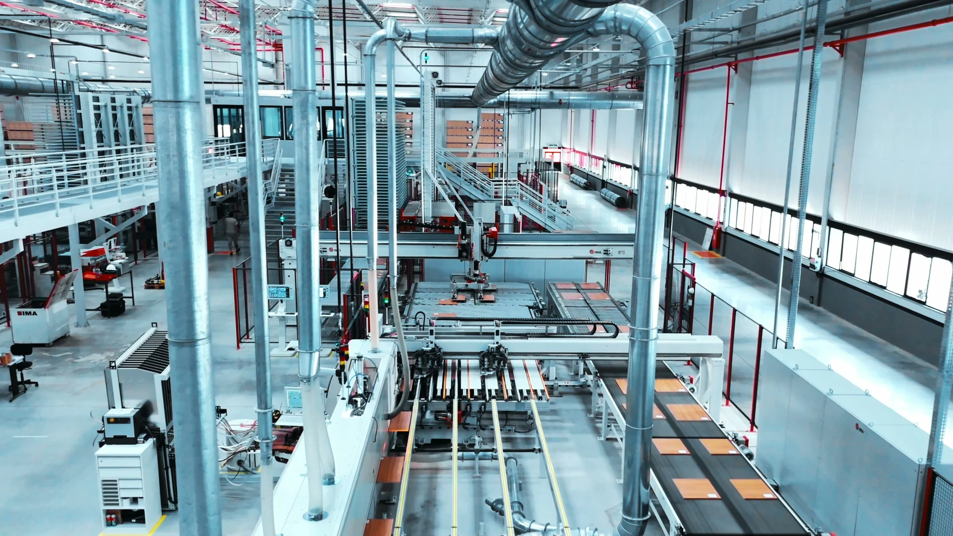 Vista elevada do interior da fábrica, com tubulações prateadas, esteiras e máquinas de linha de produção.