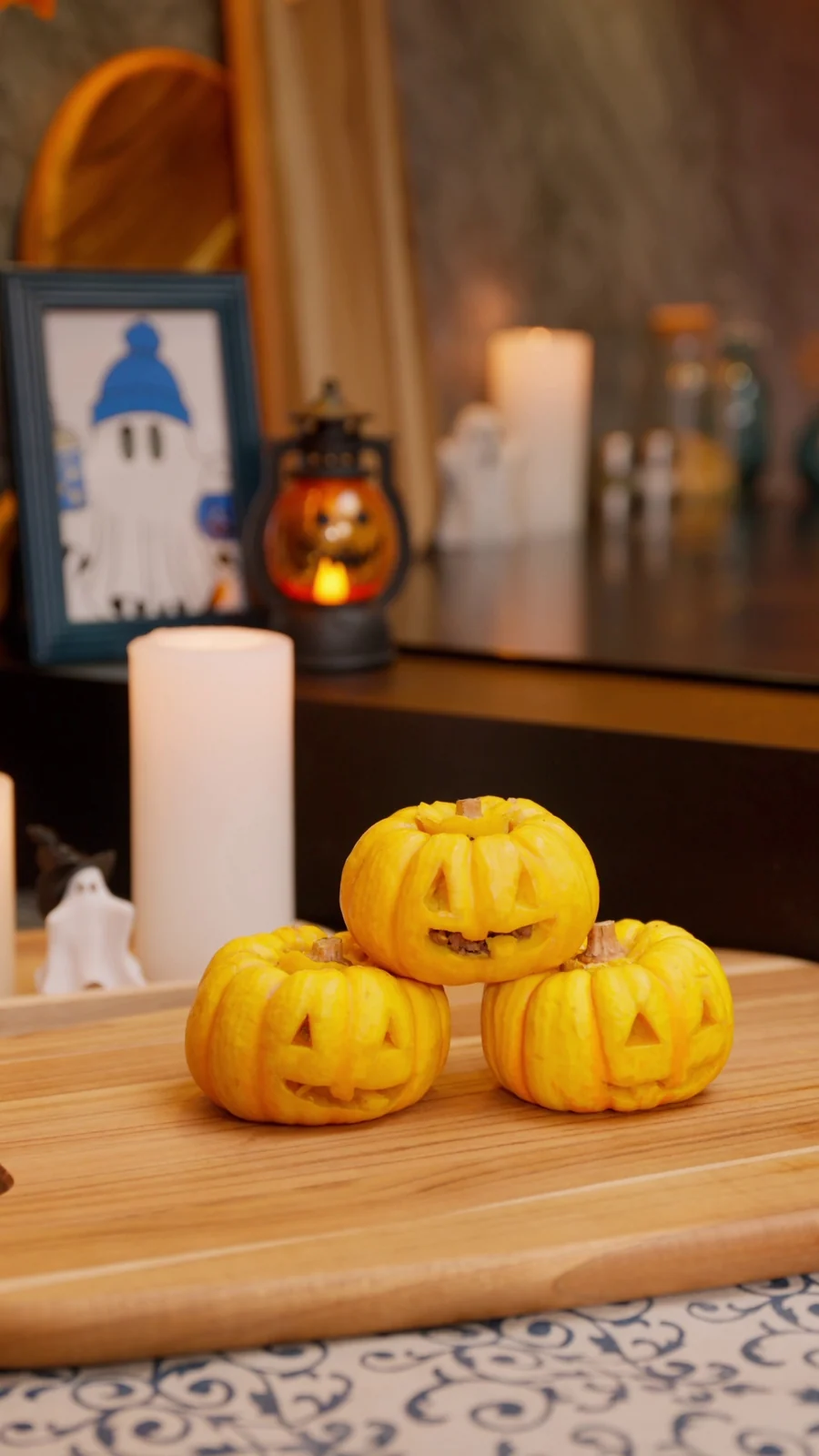 Pequenas abóboras entalhadas como lanternas de Halloween sobre tábua de madeira, com velas ao fundo.