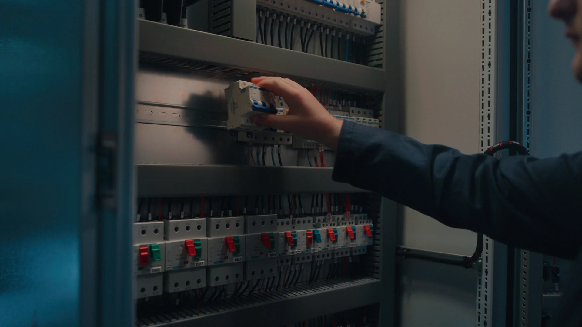 Mão encaixa um disjuntor em um quadro elétrico com fileiras de dispositivos de proteção.
