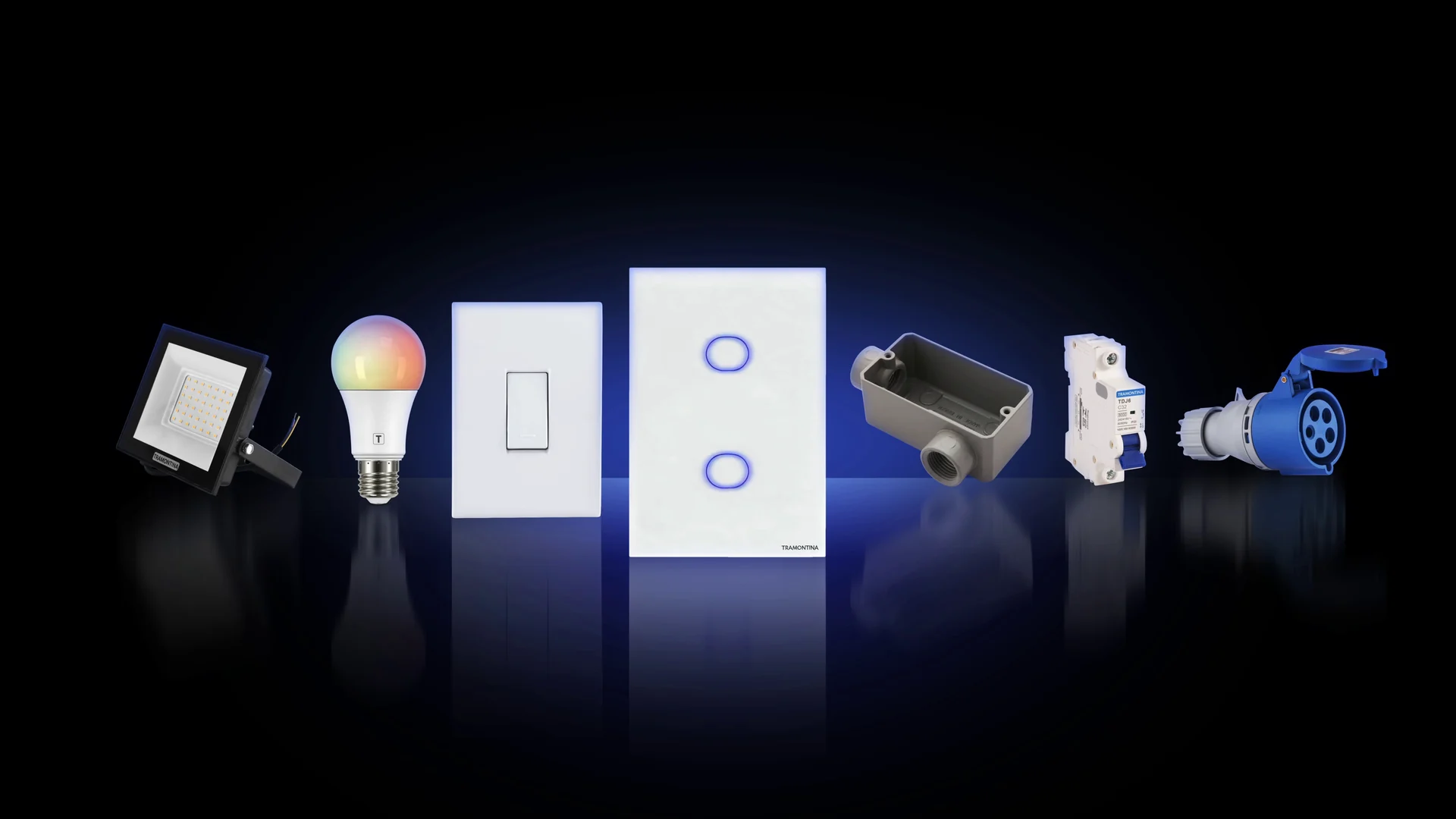 Linha de produtos Eletrik alinhada sobre fundo preto: refletor, lâmpada, interruptores, condulete, disjuntor e tomada industrial.