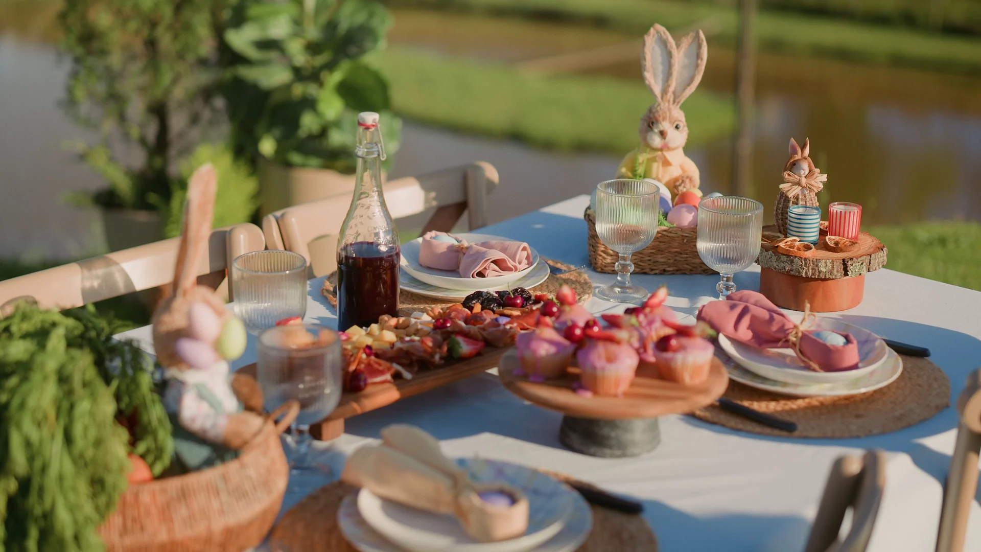 Mesa de Páscoa ao ar livre com doces, cupcakes e coelhos decorativos, diante de um lago.