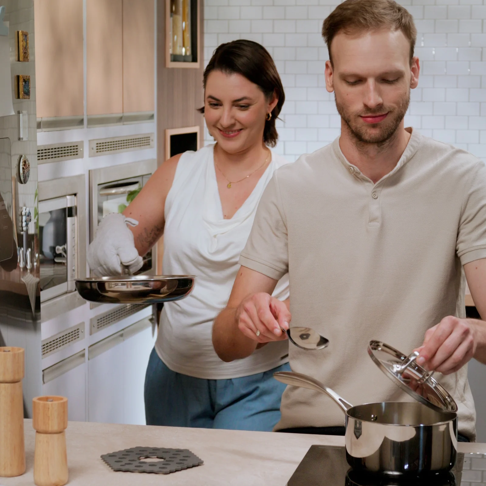 Casal cozinha junto em uma cozinha clara, com frigideira e panela de inox da linha Chrono.